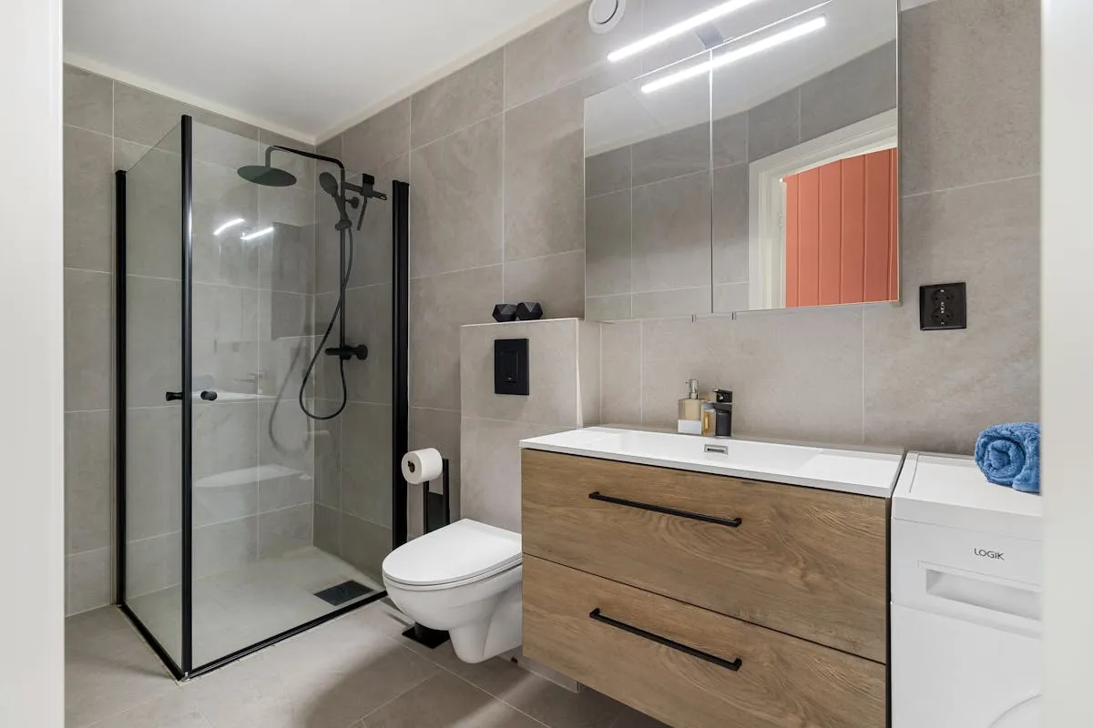 A modern bathroom with a wall-hung toilet, glass shower enclosure, and wooden vanity