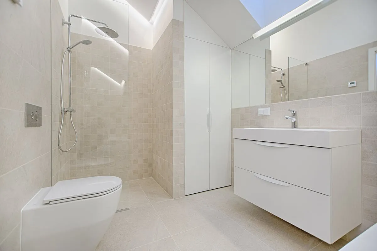 A minimalist modern bathroom with a wall-hung toilet, walk-in shower, and white vanity
